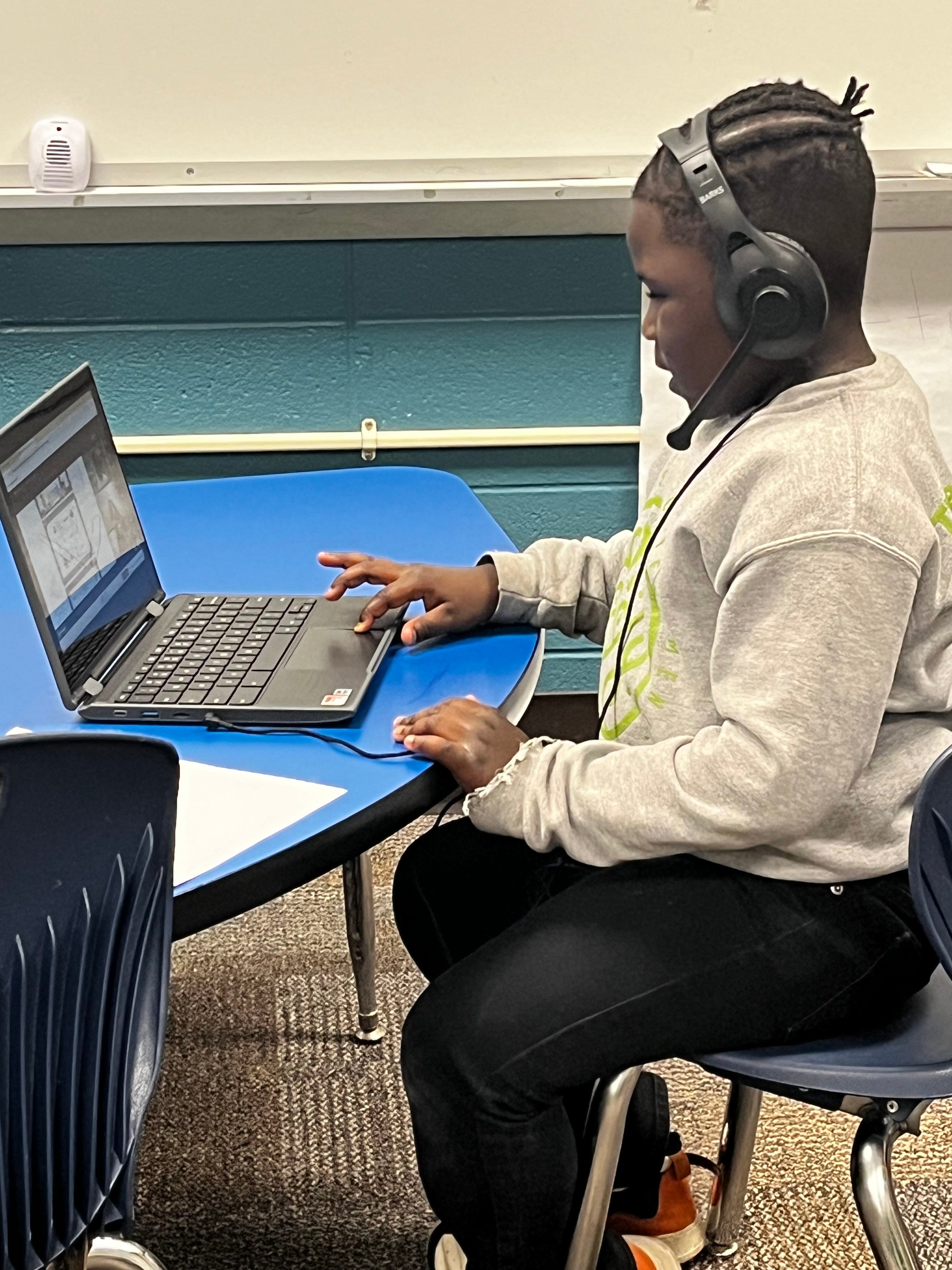 young boy sitting at a table wearing headphones and interacting with a laptop