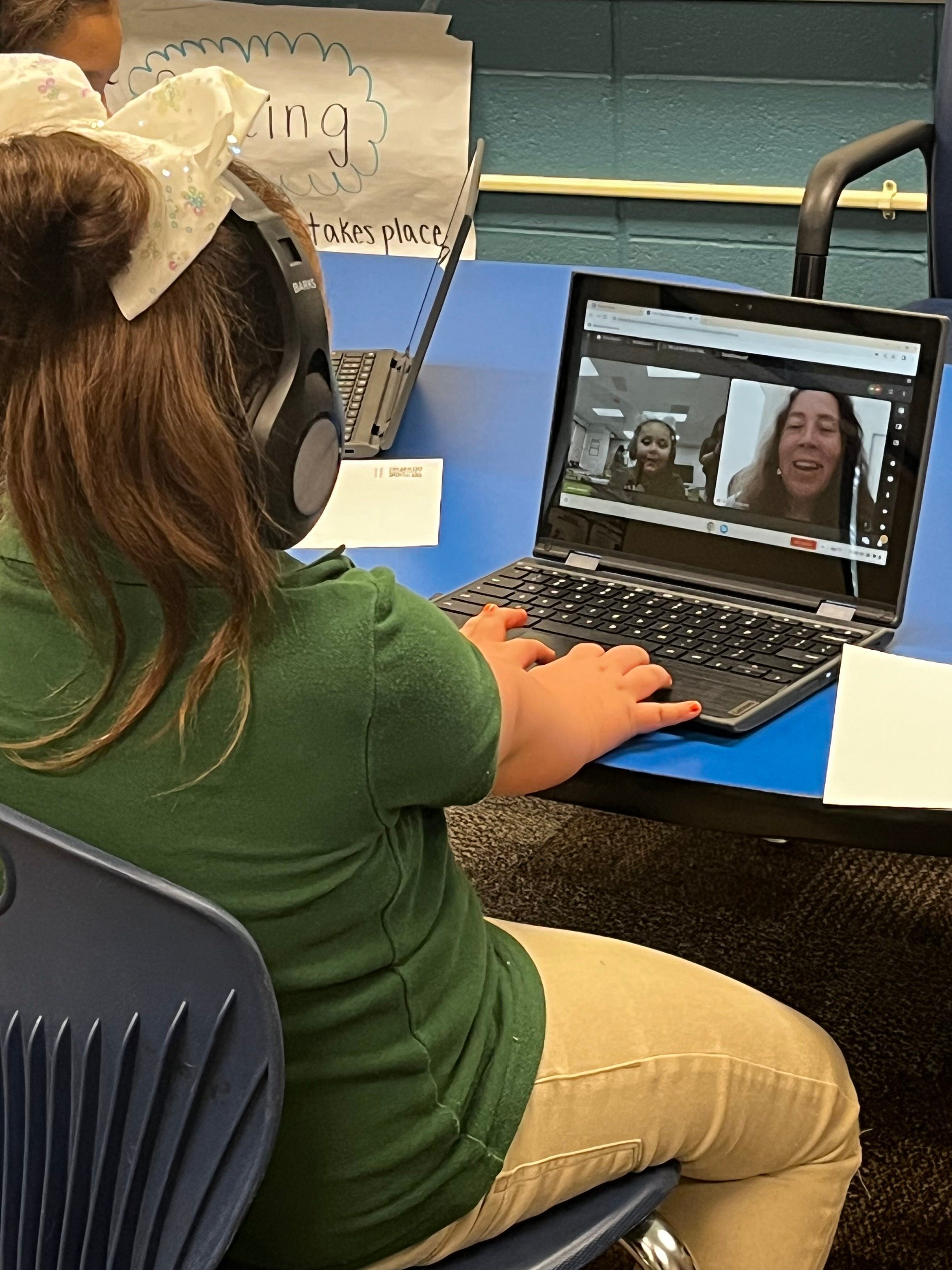 young girl wearing headphones and interacting with someone on a laptop